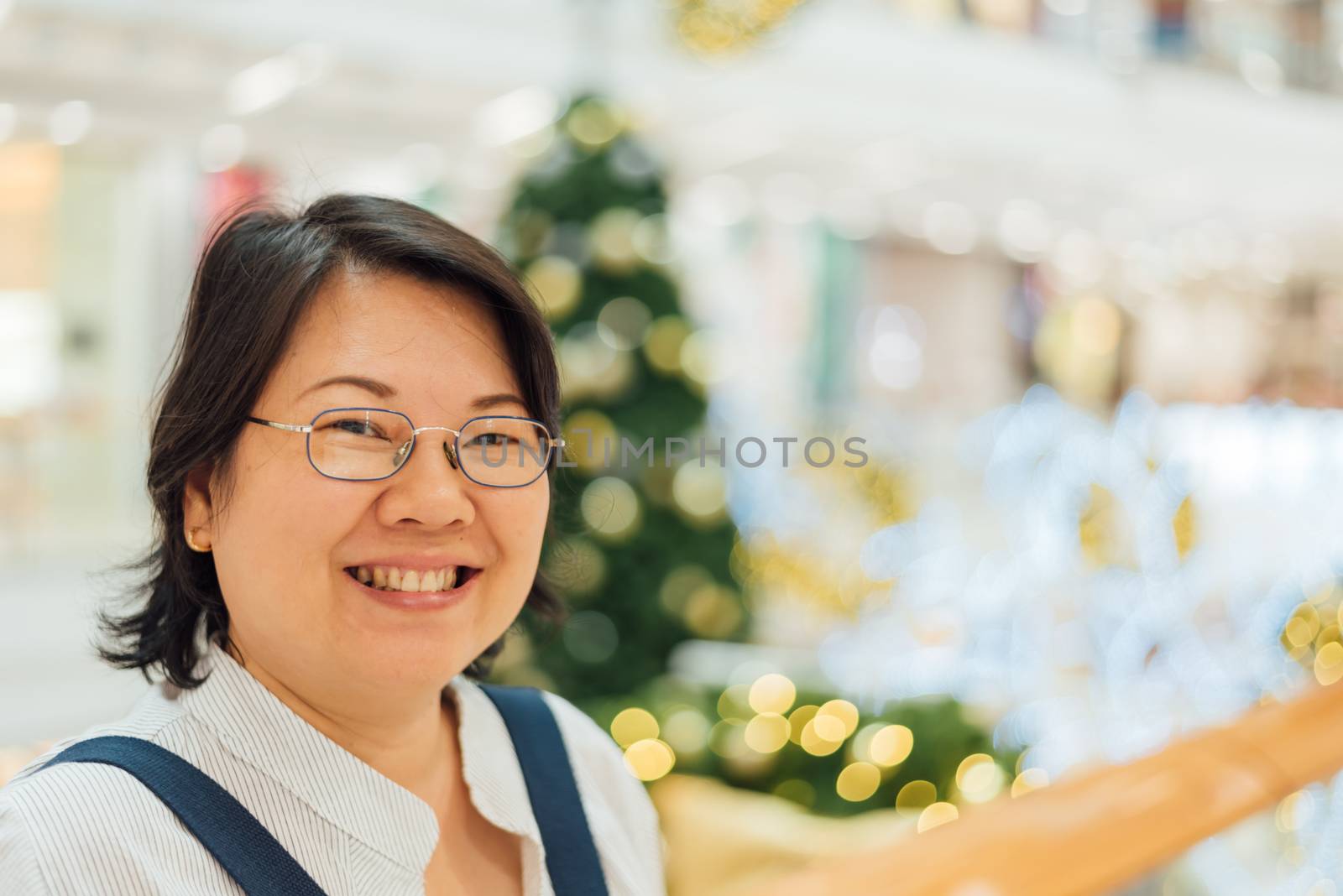 Asian woman 40s white skin plump body with backpack waiting in department store or shopping mall with pine tree in merry christmas and new year celebration