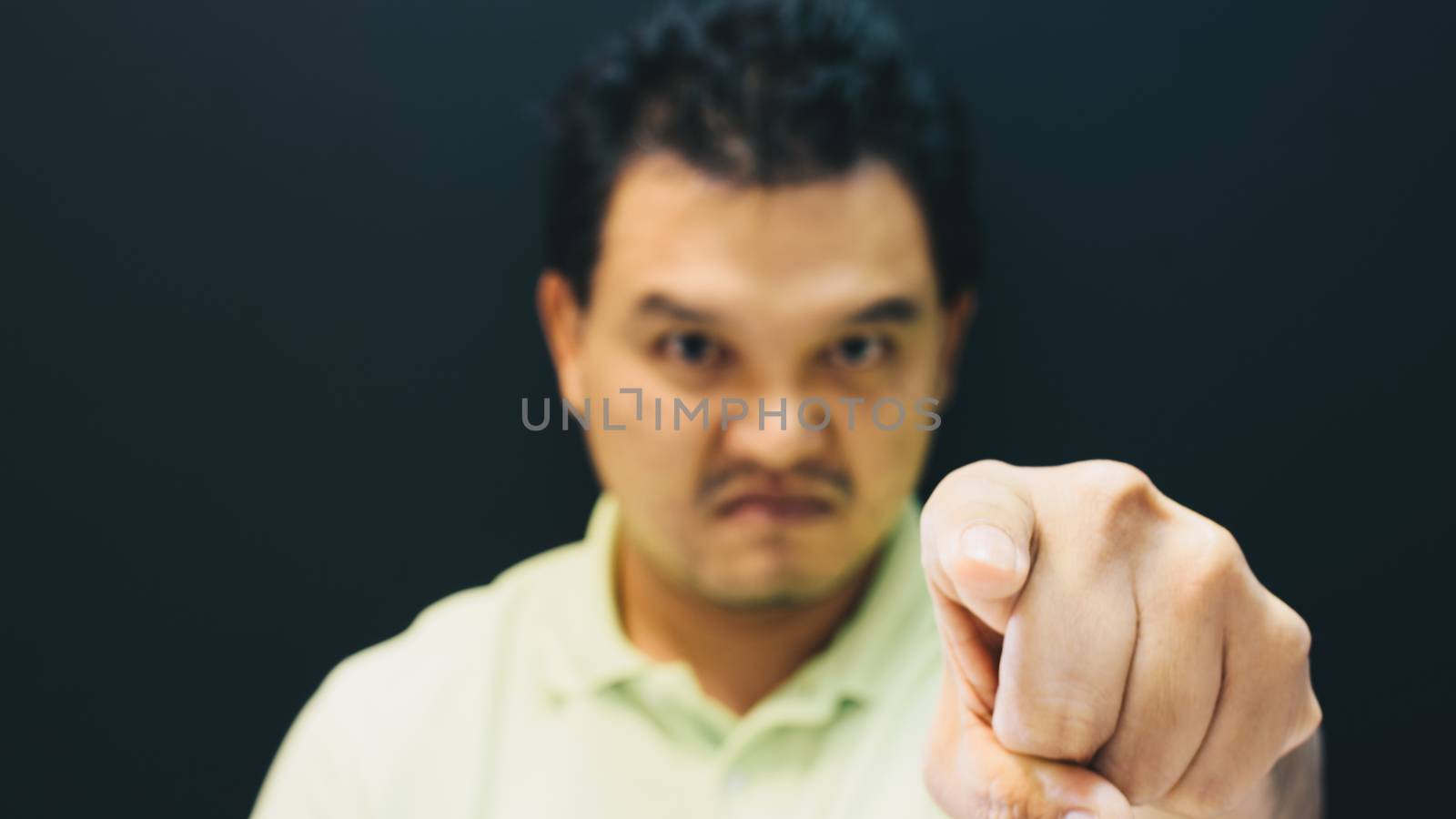 Asian man 40s in green polo shirt do finger pointing at you with anger and crazy gesture in angry or blame concept on black background dark style (Focus on finger)