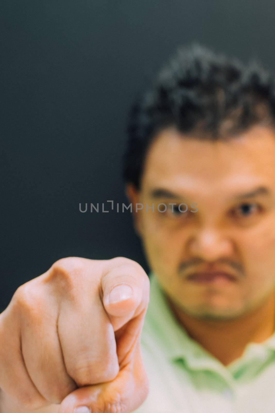 Asian man 40s in green polo shirt do finger pointing at you with anger and crazy gesture in angry or blame concept on black background dark style (Focus on finger)