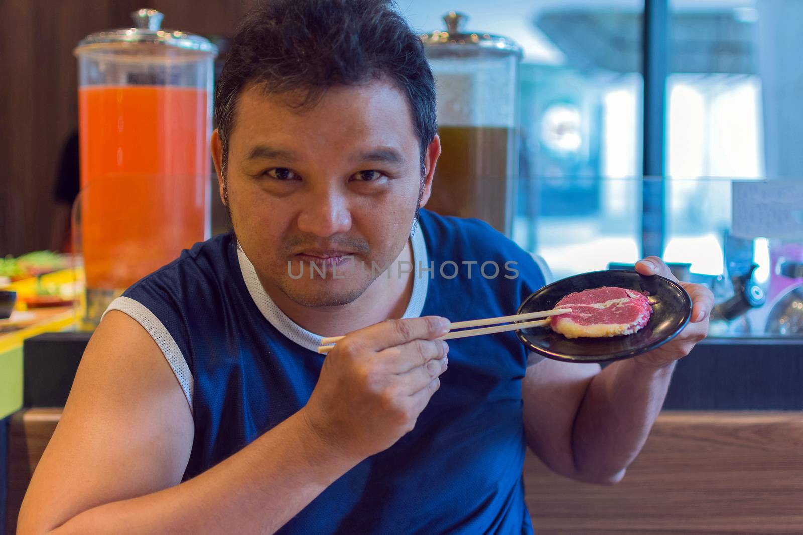 Asia man plump body holding a beef in dish with chopsticks, defocus blurred on BBQ. yakiniku grill buffet restaurant background.