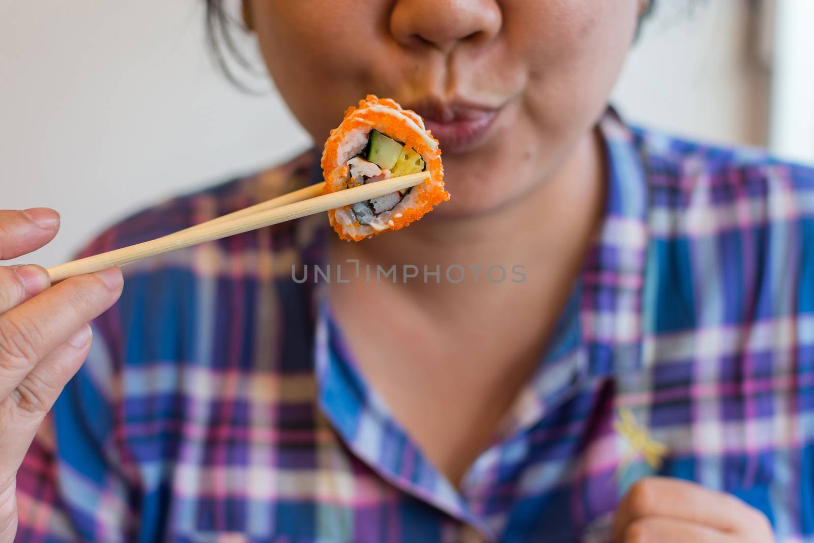 Asia woman plump body holding chopsticks with a california roll in japanese food buffet restaurant.