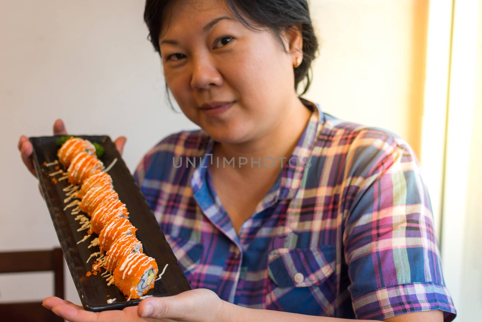 Asia woman plump body holding california roll on dish in japanese food buffet restaurant. , process in soft orange sun light style