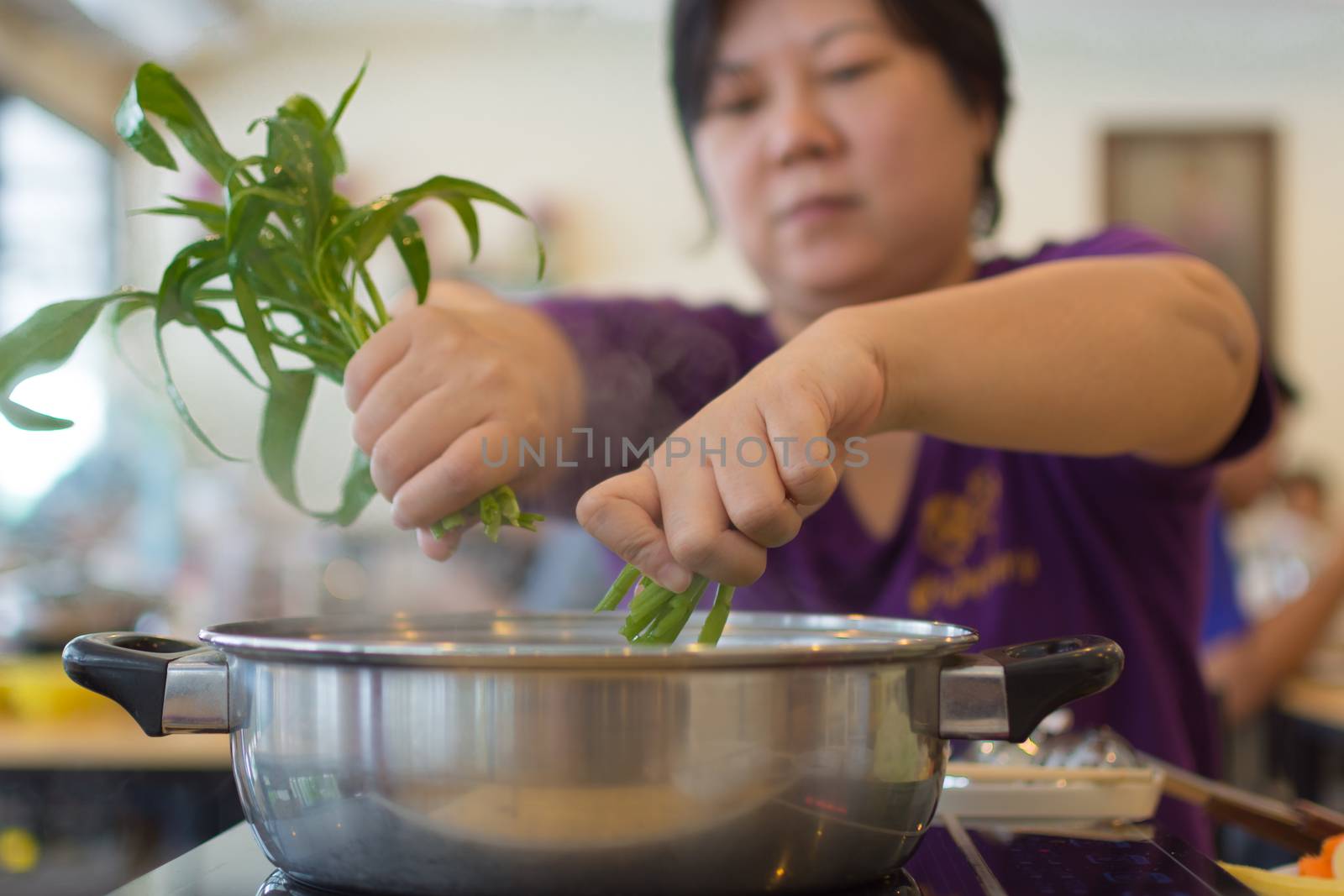 Asia woman plump body cooking food by put a vegetable (morning glory) in to a hot pot for make a sukiyaki or shabu