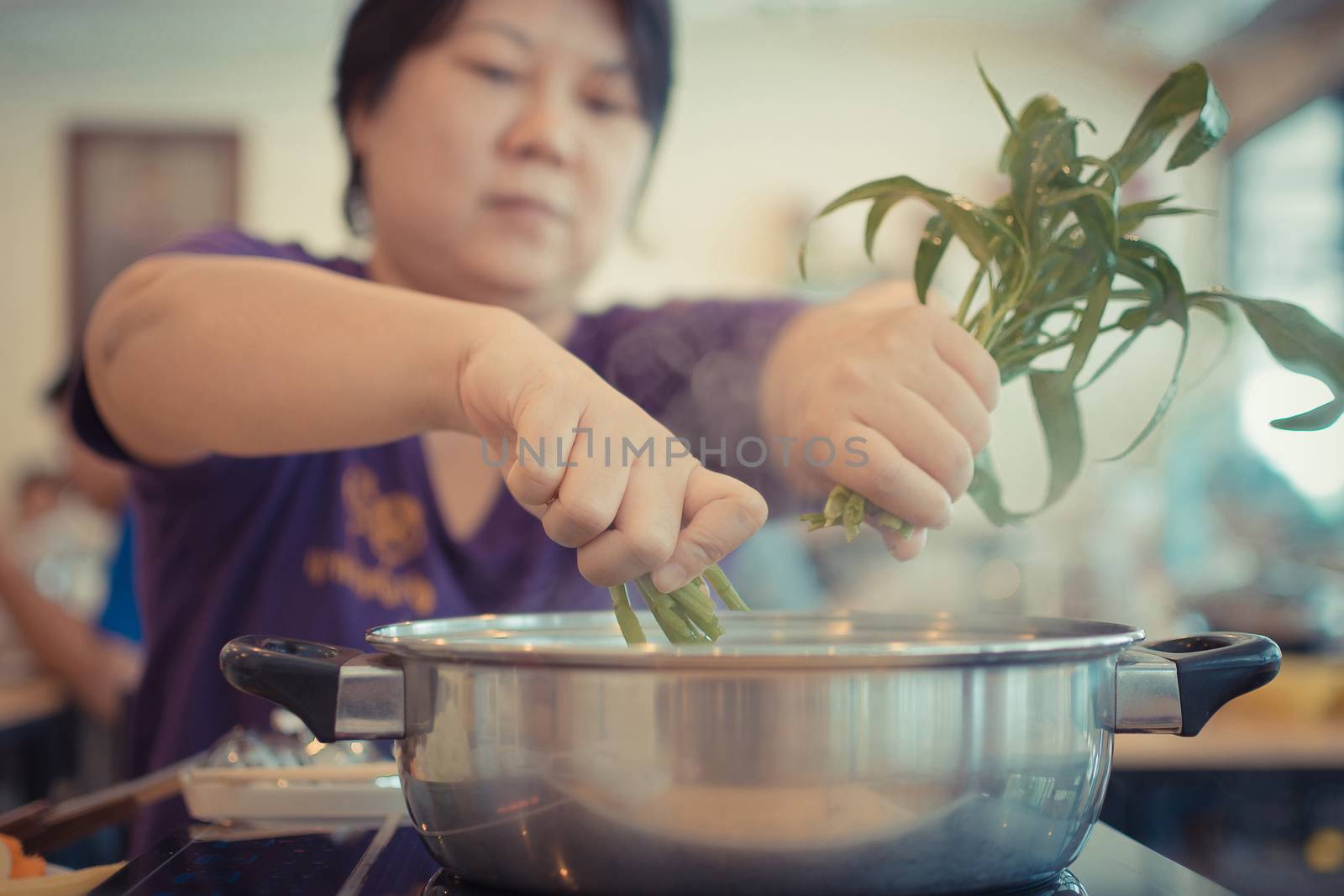 Asia woman plump body cooking food by put a vegetable (morning glory) in to a hot pot for make a sukiyaki or shabu , process in vintage style