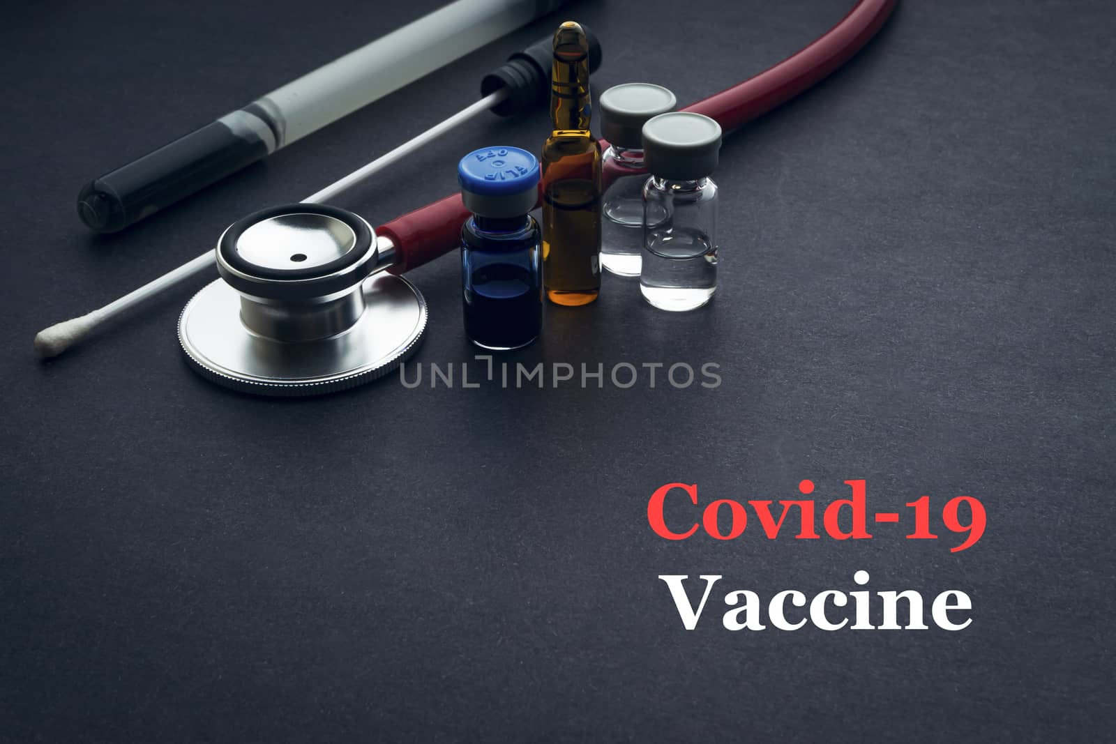 COVID-19 or CORONAVIRUS VACCINE text with stethoscope, medical swab and vial on black background. Covid-19 or Coronavirus concept. 