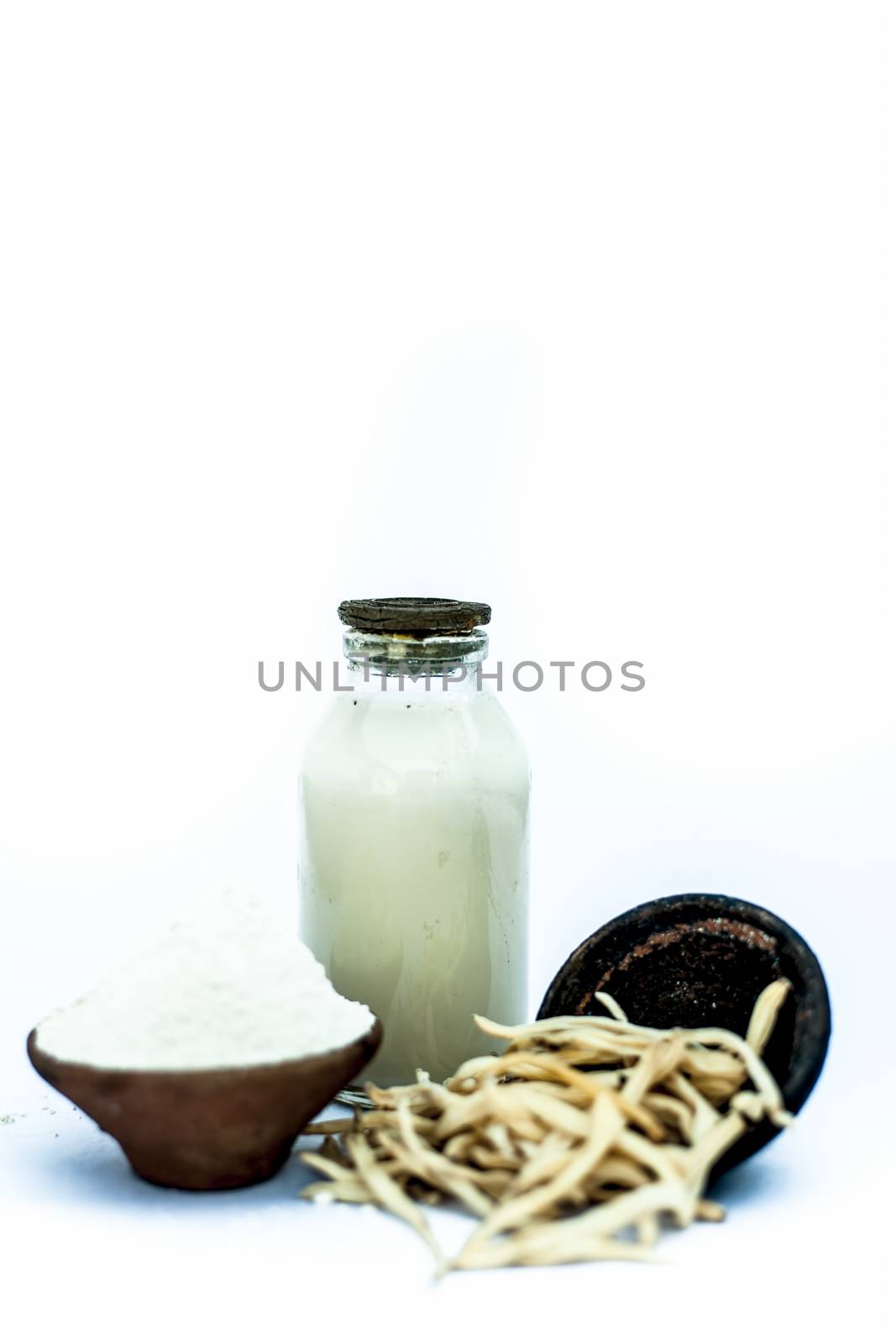 Popular Indian & Asian ayurvedic herb isolated on white in a clay bowl i.e. Musli or safed musli or Chlorophytum borivilianum with its powder in a clay bowl and raw milk in a transparent glass bottle.
