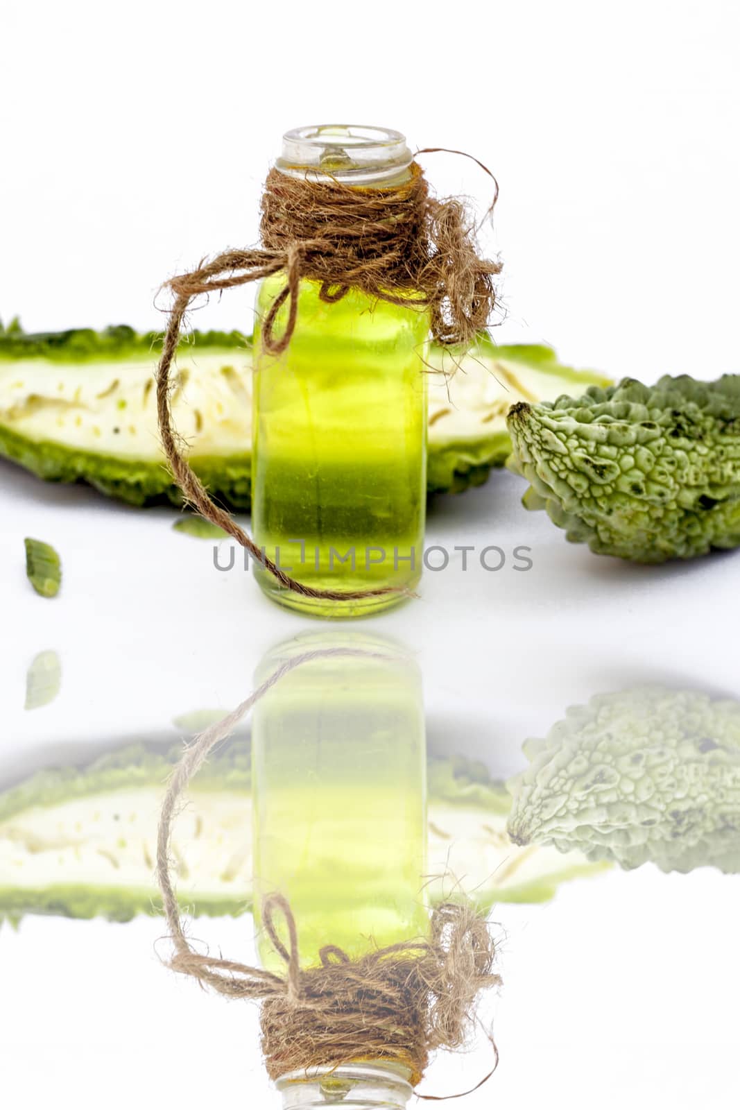 Raw organic bitter melon or Bitter Cucumber or Bitter Gourd isolated on white along with its detoxifying essential oil in a transparent glass bottle,with its reflection.