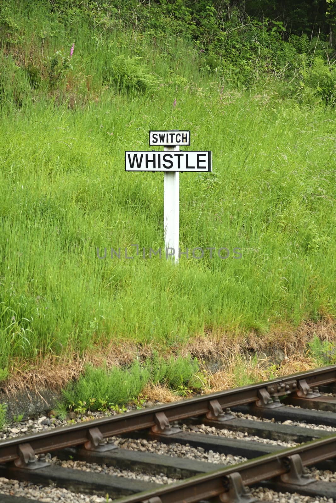 The view across railway track towards a sign requiring oncoming trains to blow their whistle.