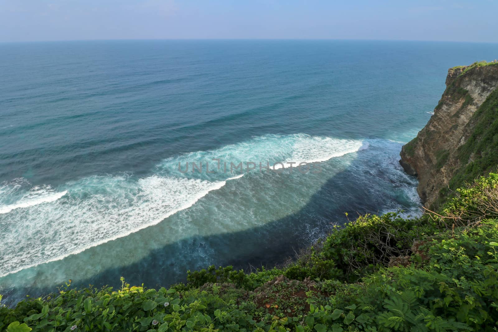 Overview panorama ocean shore, cliff. Overwhelmed scene the flower and green-capped vertical cliff over the Indian ocean. South of Bali island, Pura Luhur Uluwatu Temple. Indonesia.