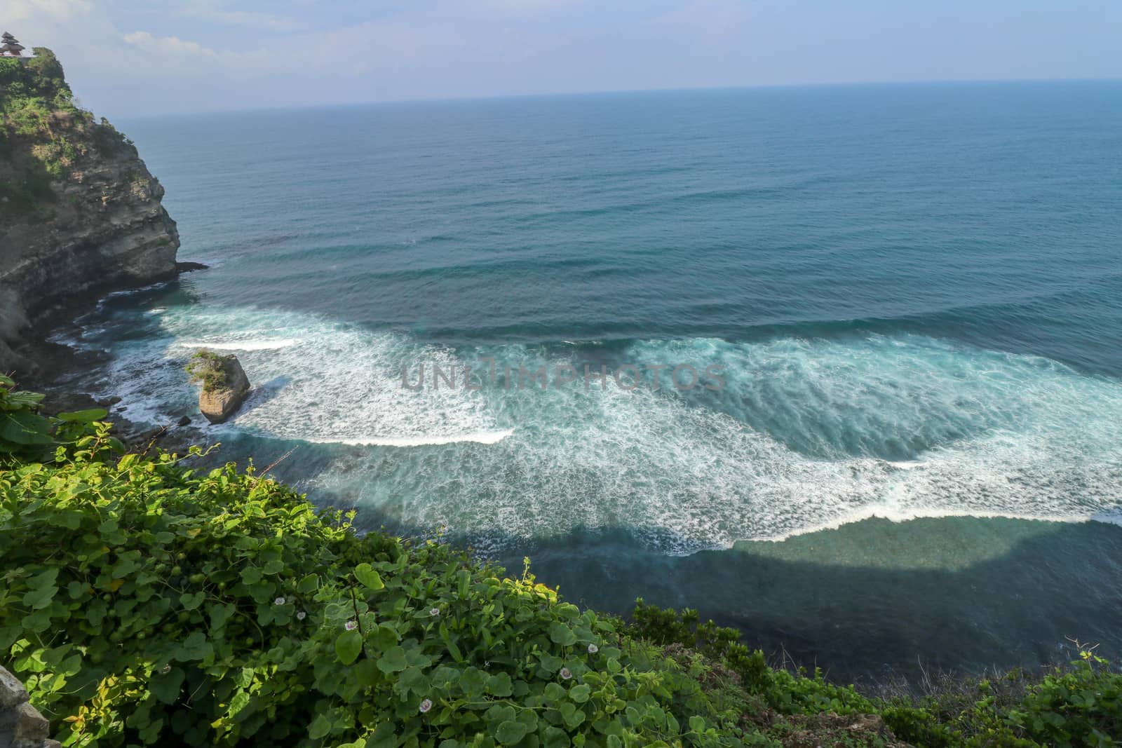 Overview panorama ocean shore, cliff. Overwhelmed scene the flower and green-capped vertical cliff over the Indian ocean. South of Bali island, Pura Luhur Uluwatu Temple. Indonesia.