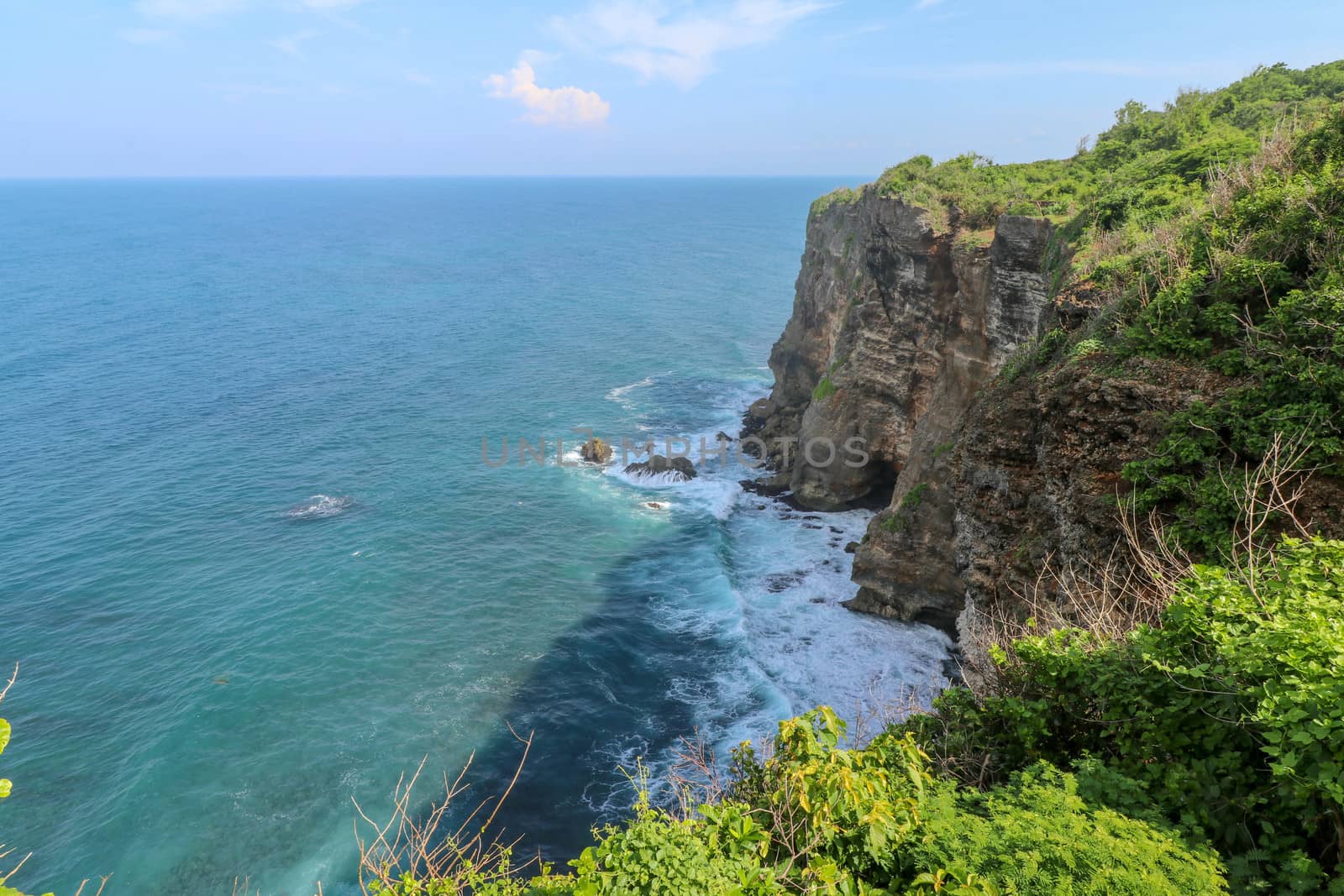 Overview panorama ocean shore, cliff. Overwhelmed scene the flower and green-capped vertical cliff over the Indian ocean. South of Bali island, Pura Luhur Uluwatu Temple. Indonesia.