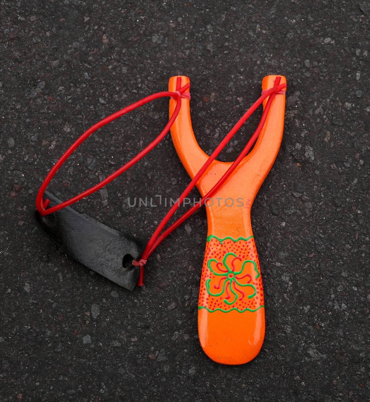 Handmade orange slingshot catapult. Y-shaped wooden stick with elastic tied between two top parts. Slingshot or Catapult is a device for shooting small stones.