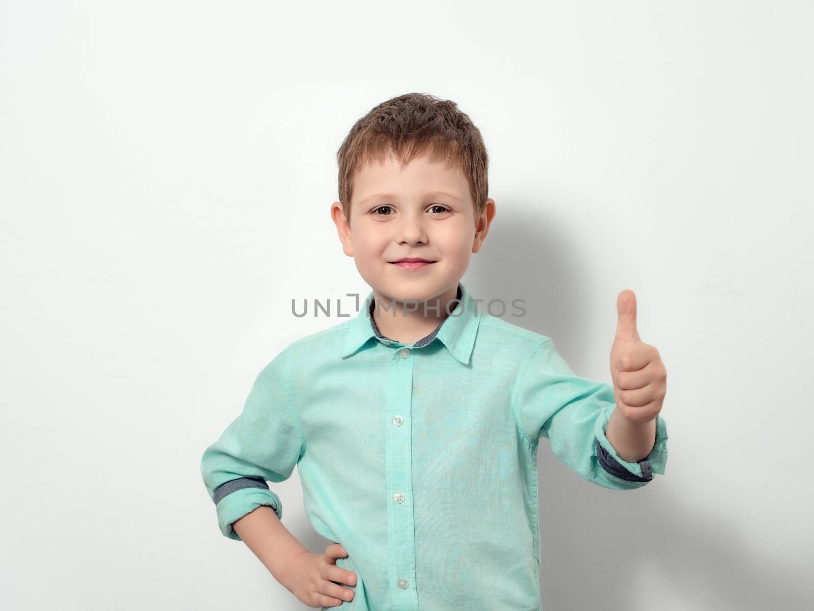 Four-year-old boy smiles and shows thumb up. Happy child in blue shirt, isolated on white background.