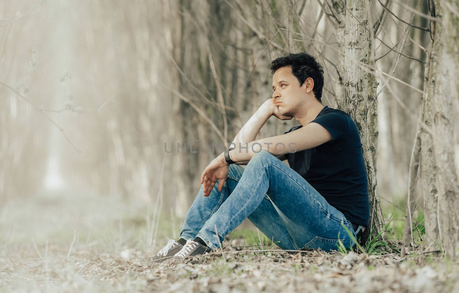young man sitting by a tree in the woods thinking about life and resting