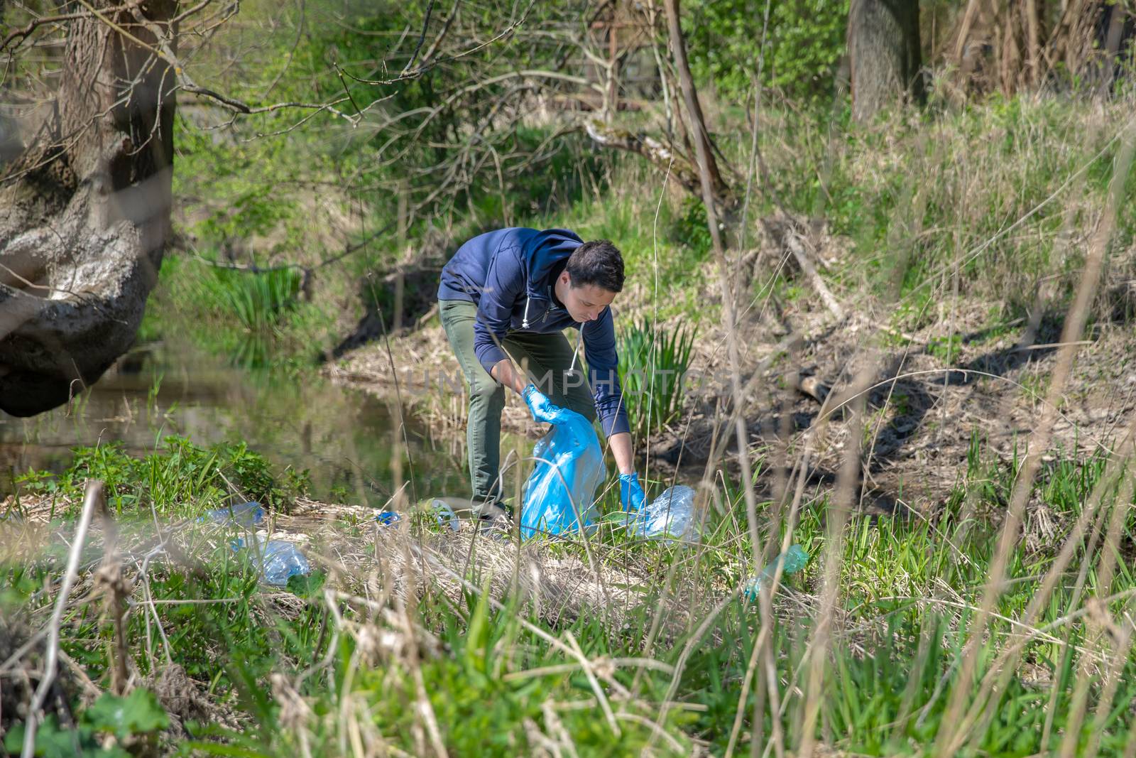 collecting garbage in a plastic bag, a volunteer man helps in the forest on the river bank by Edophoto