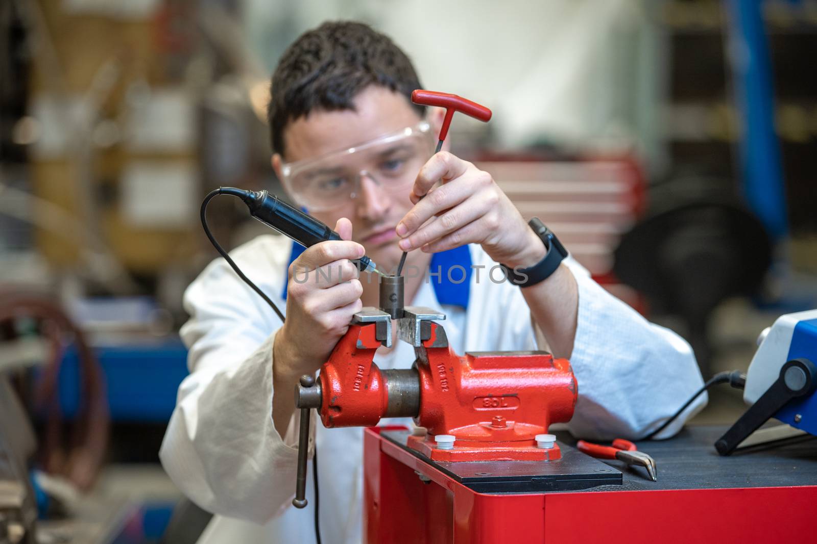 young technician in a factory repairing a machine. man uses a vise to work in the factory.