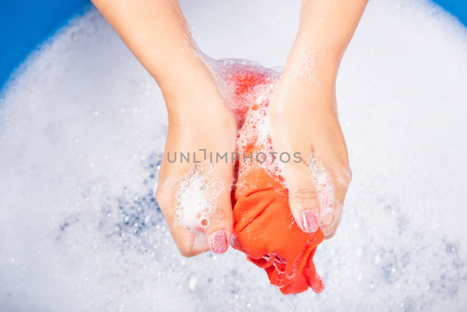 Closeup young Asian woman use hands washing color clothes in basin with detergent have soapy bubble water, studio shot background, laundry concept