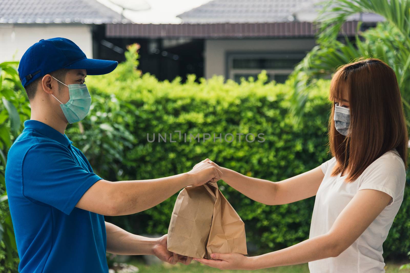 Asian delivery express courier young man giving paper bags fast food to woman customer receiving both protective face mask, under curfew quarantine pandemic coronavirus COVID-19