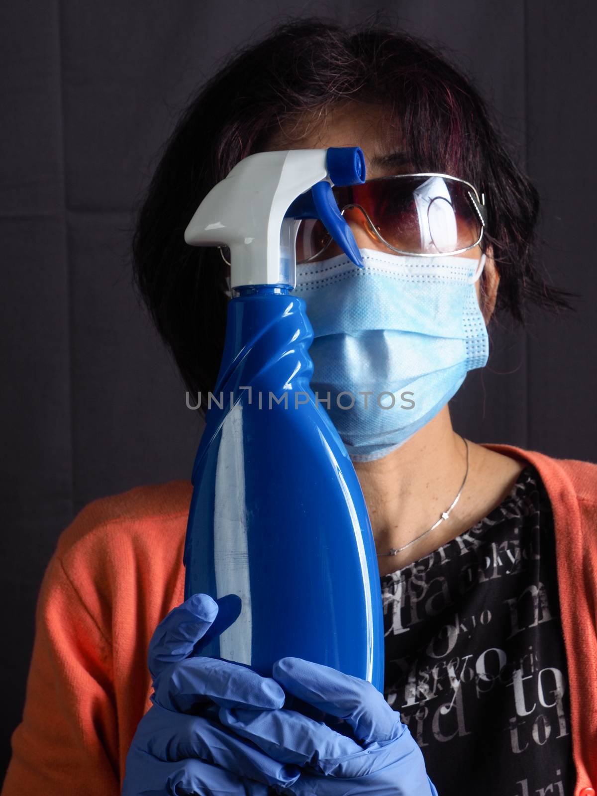 funny humorous adult asian 40s 50s woman wearing protection surgical face mask , blue latex gloves, and sun glasses pointing the head with blue sanitizer cleaning  bottle as a weapon as tired of confinement covid concept.