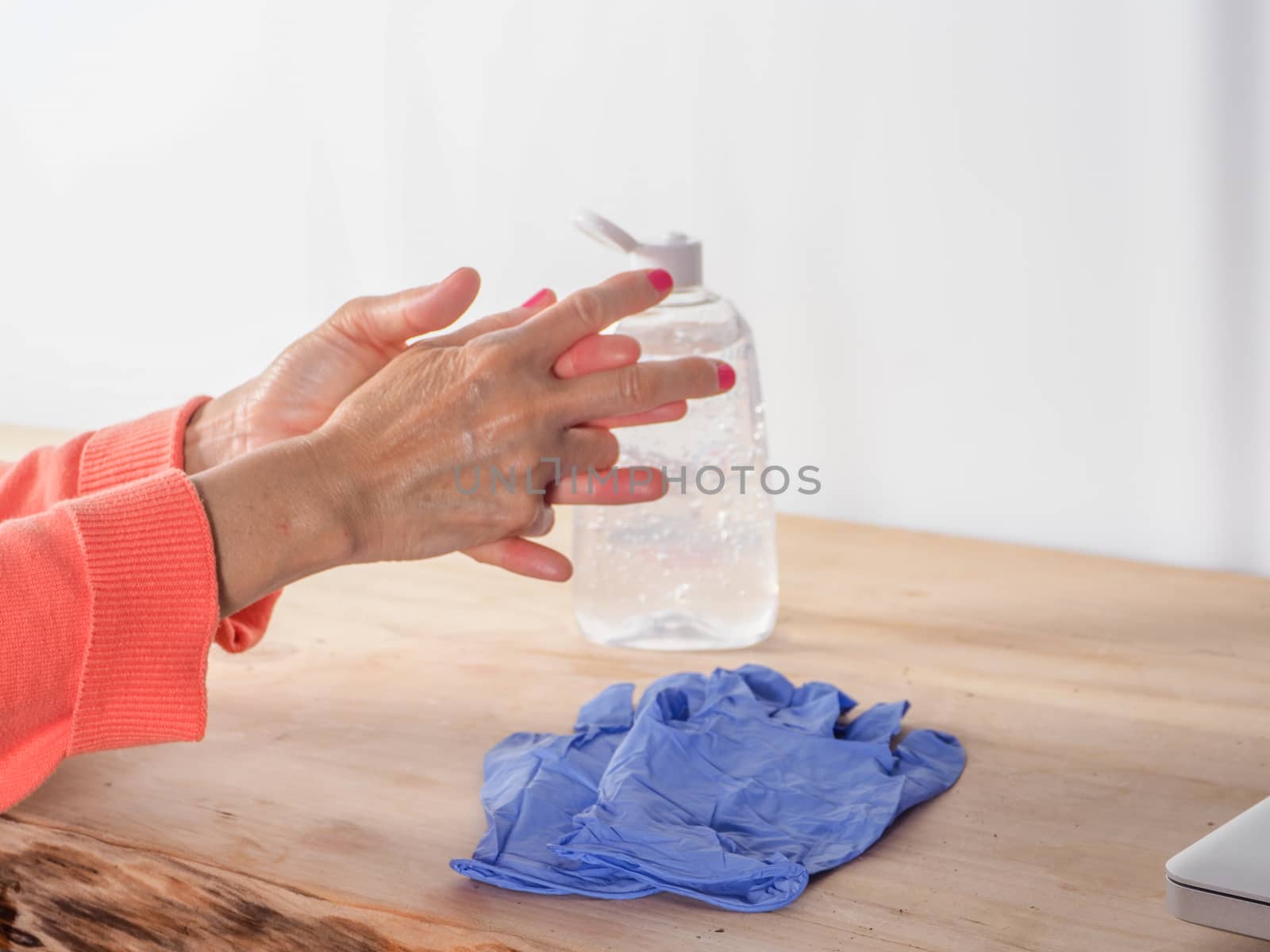 close up of  woman hands while cleaning and sanitizing  herself  with anti virus bacterial gel against covid-19 , fall dress, orange color over a wood table, earth tones.