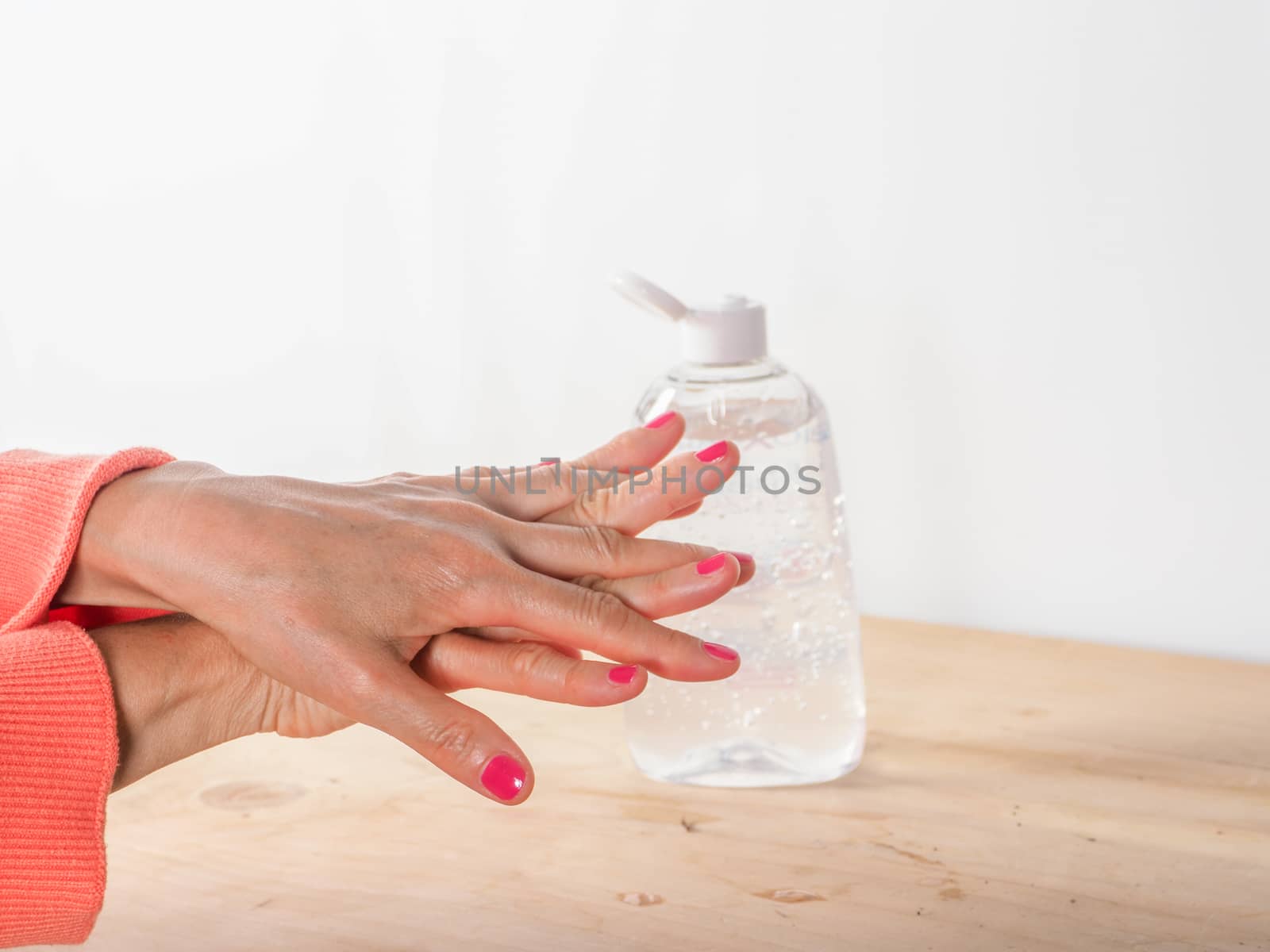 close up of  woman hands while cleaning and sanitizing  herself  with anti virus bacterial gel against covid-19 , fall dress, orange color over a wood table, earth tones.