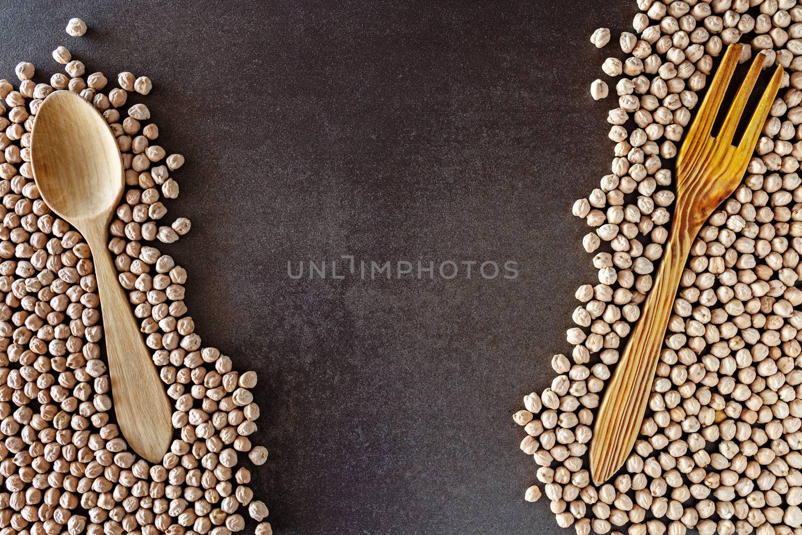 Composition of natural chickpeas with kitchen utensils, spoon and wooden fork on rustic textured bottom. View from above with space to write