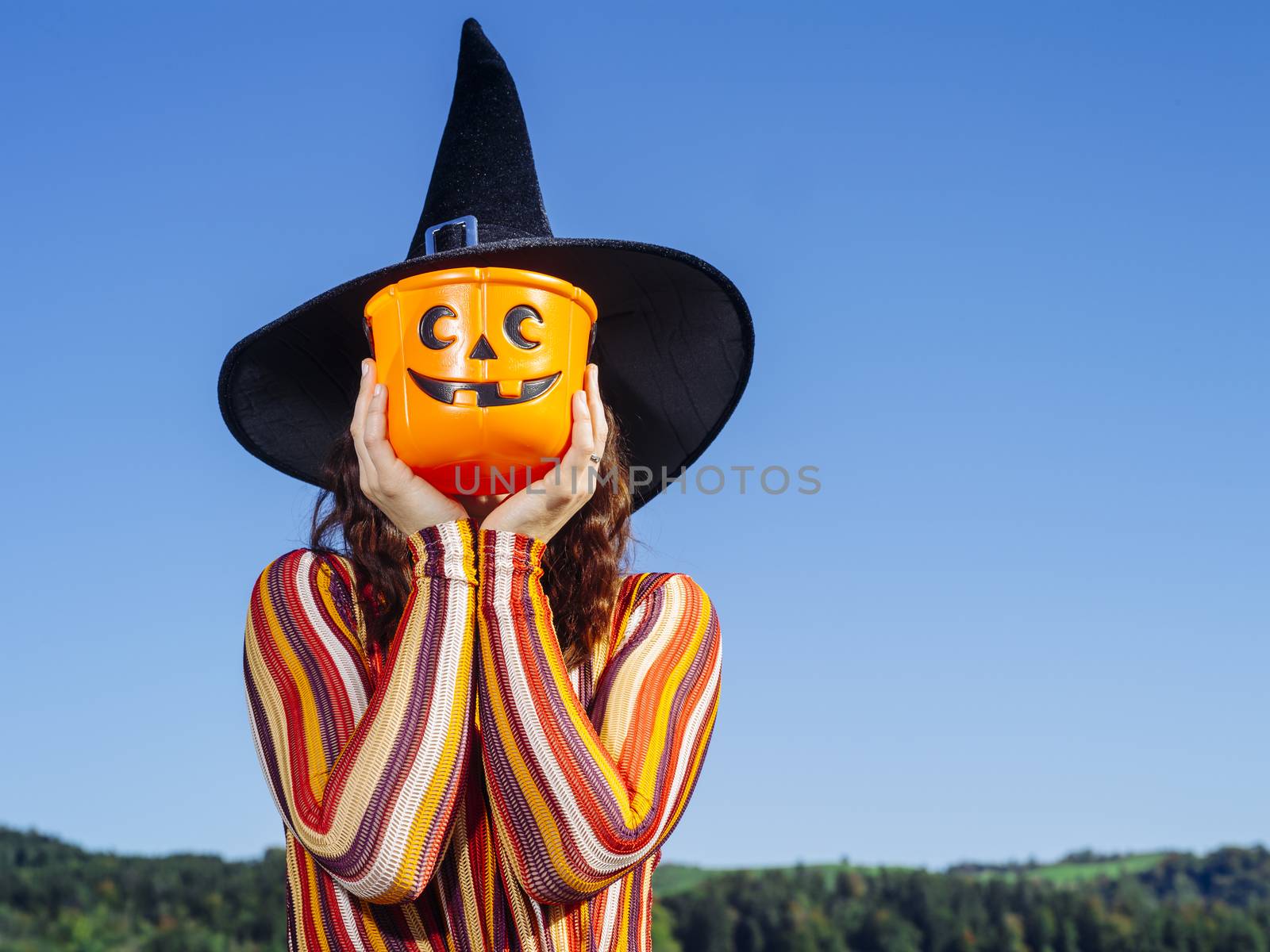 Photo of a young sexy woman holding a pumpkin candy bucket over her face for Halloween theme.