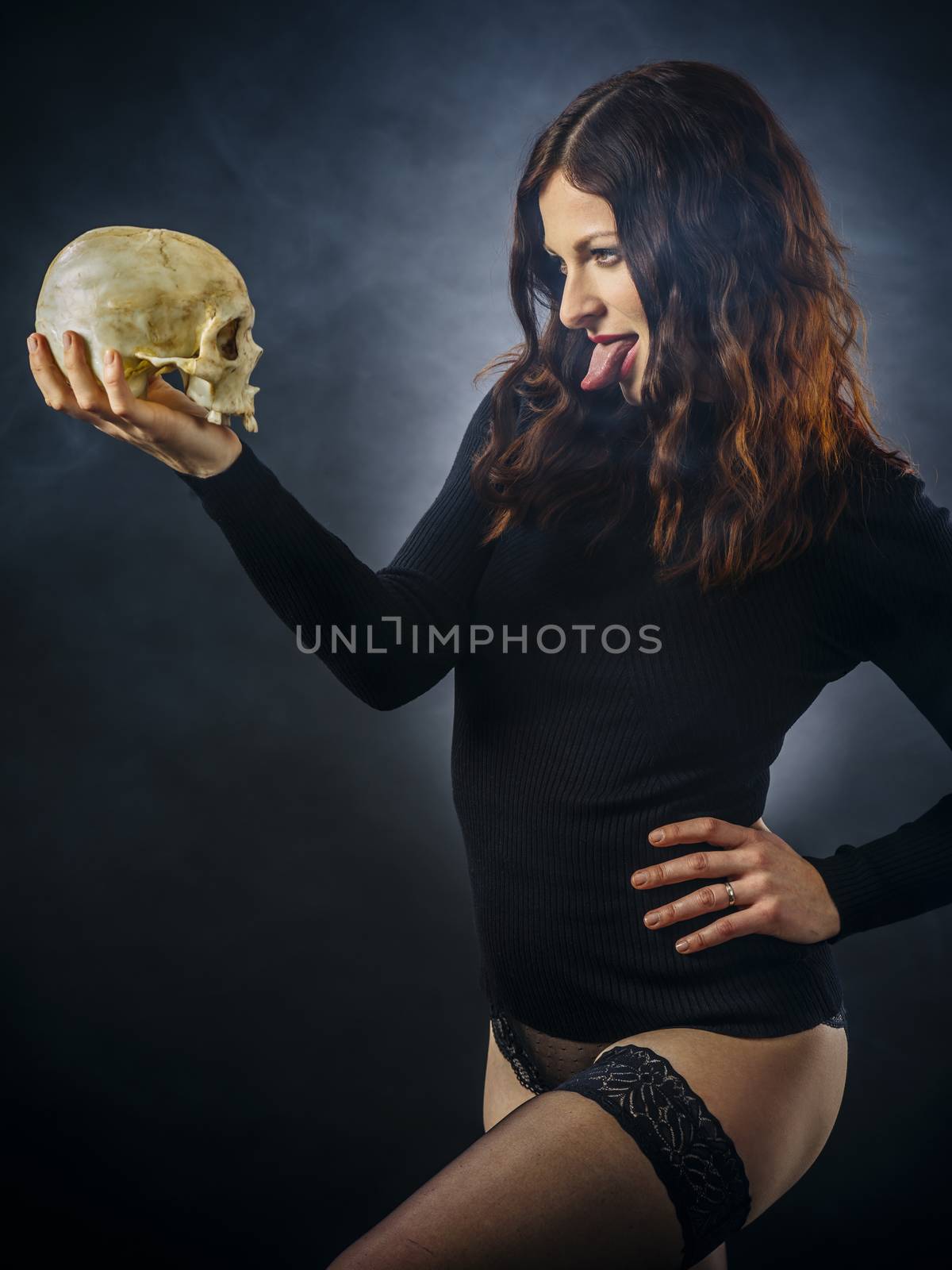 Redhead young woman sticking out her tongue at skull over dark background.