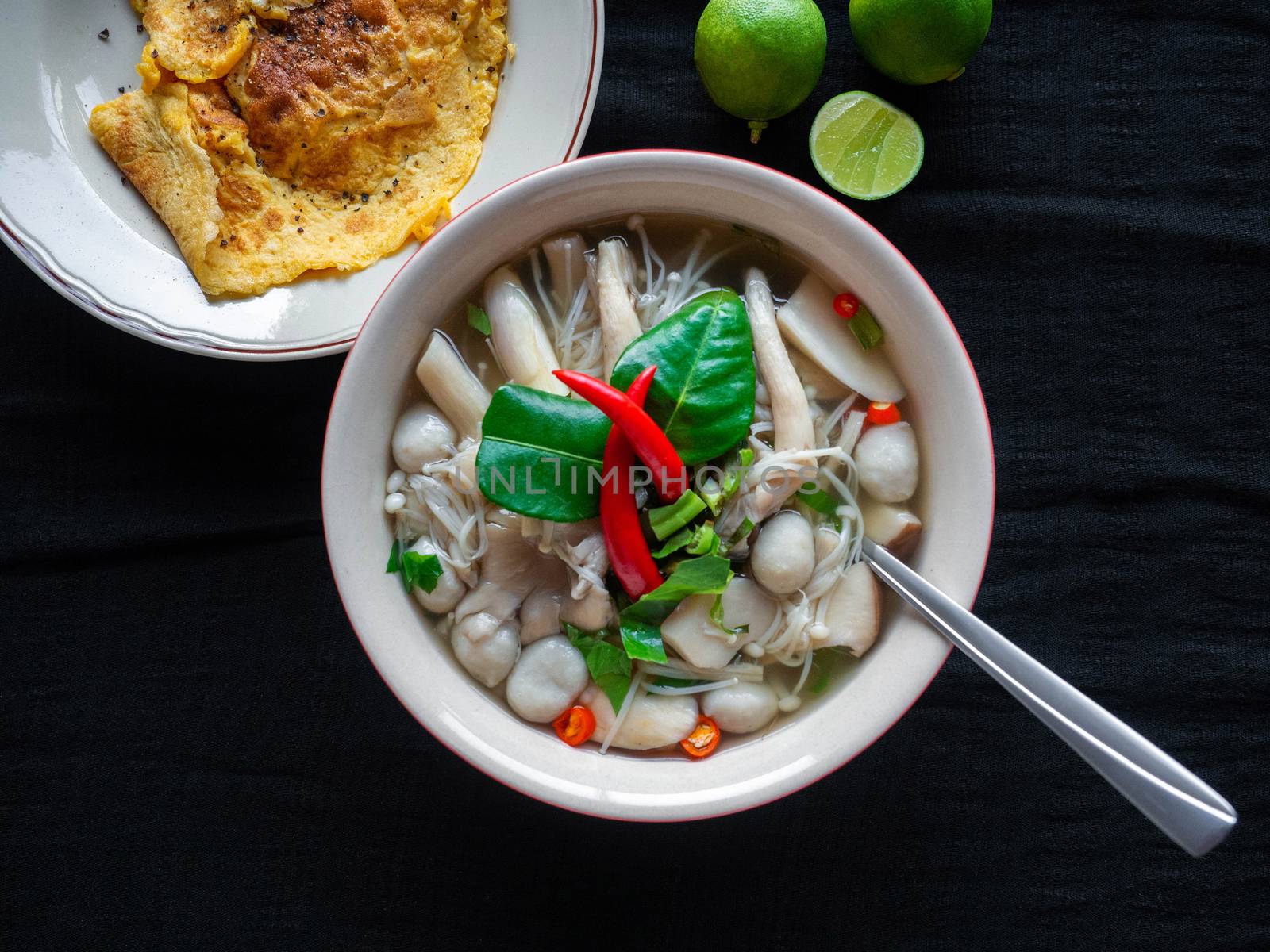 Food Thai name is Mushroom Tom Yum,Ingredients mushroom chilli lemon lemon grass Kaffir lime leaves Galangal and Coriander,saw blade,Black fabric background,Omelette, side dish