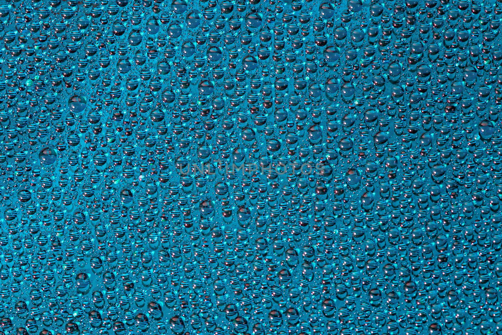 water drops on aurora green pearl glass of modern phone back cover, close-up with selective focus and blur.