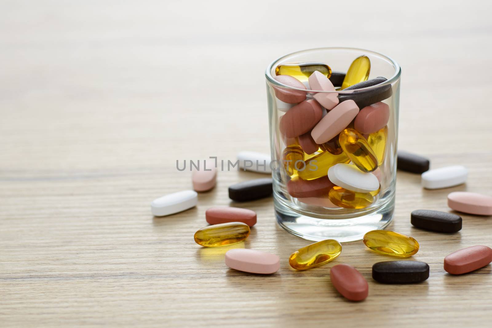 Fishoil capsules and Multivitamin supplements in the small glass on the wooden table with copy space.