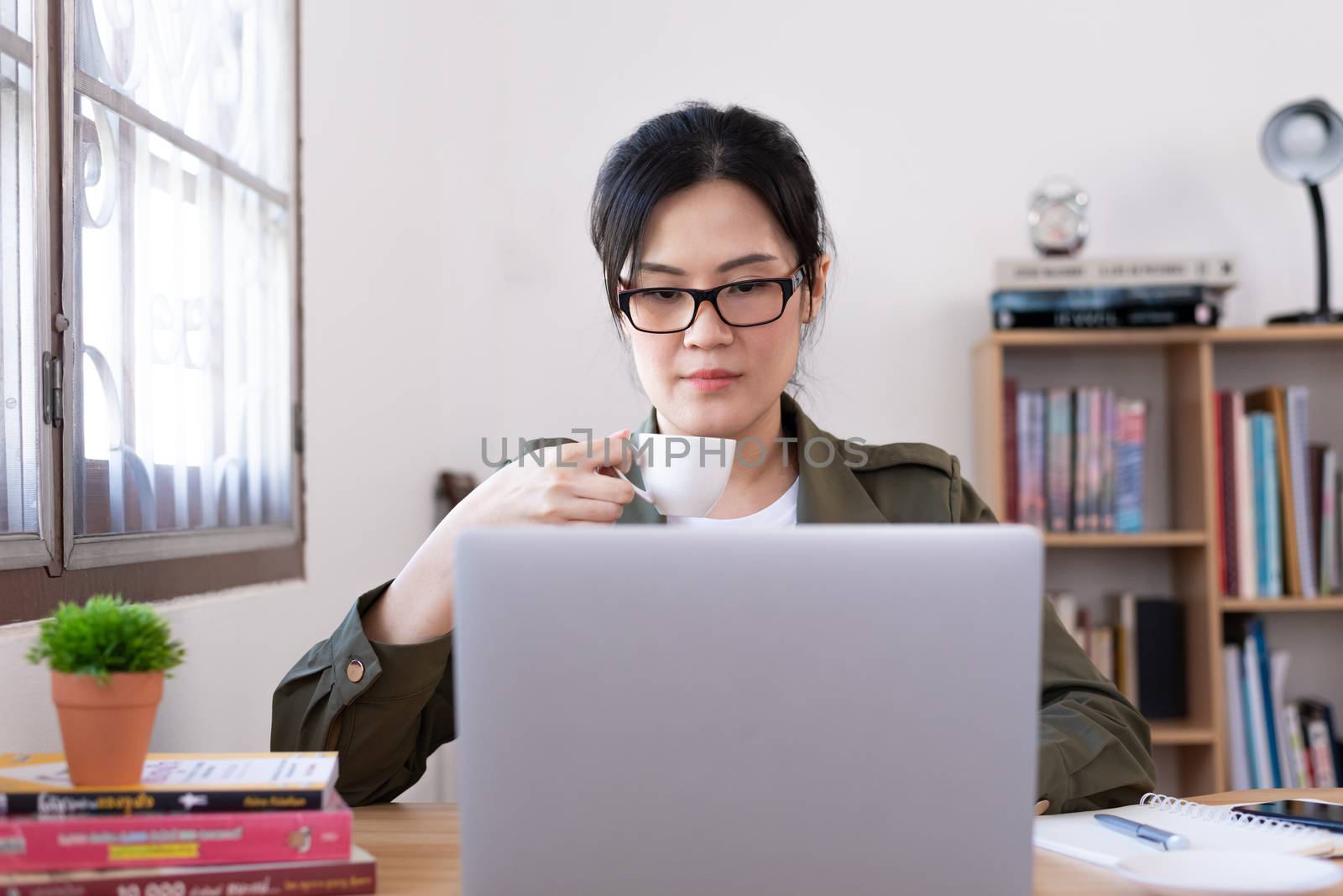 Modern young Asian woman working from home and drinking a coffee by animagesdesign