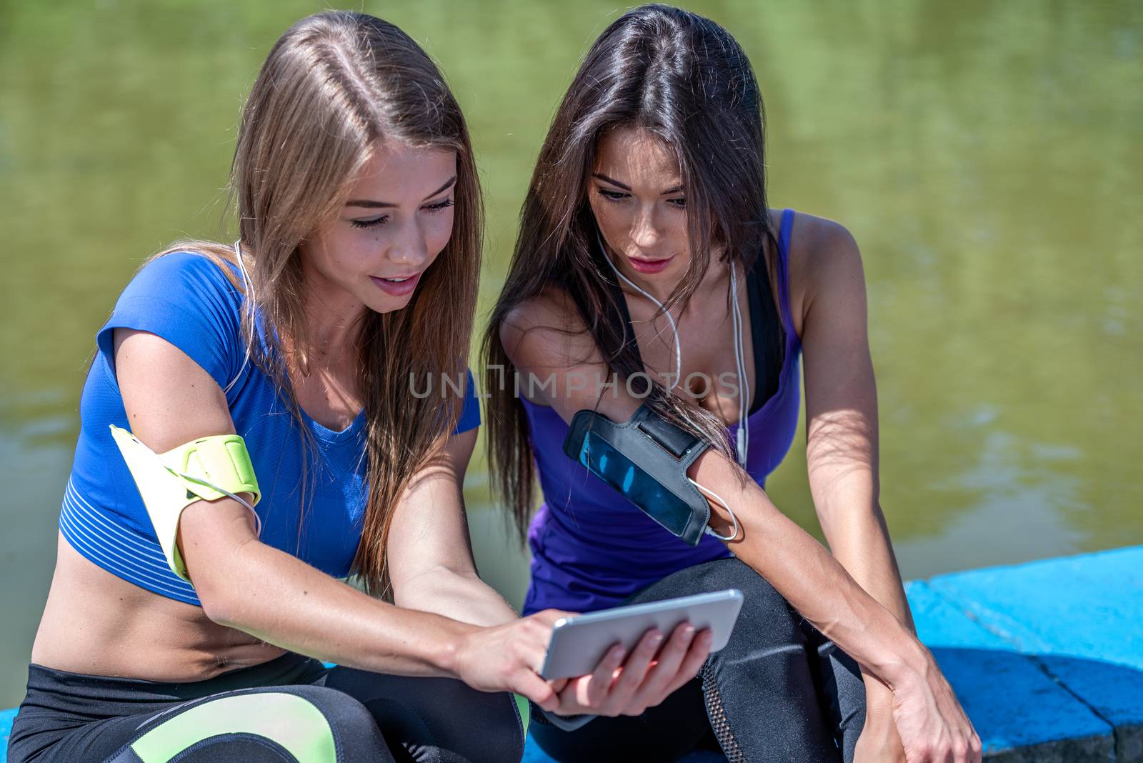 Young attractive fitness girls talking about their workout and checking sport application details on the smartphone