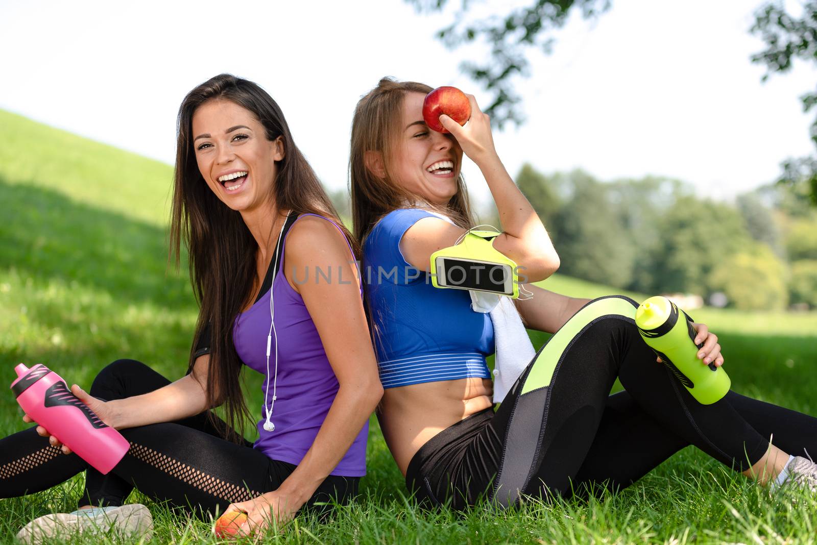 Portrait of two cute girls relaxing and smiling after outdoors exercises in the park on a sunny day