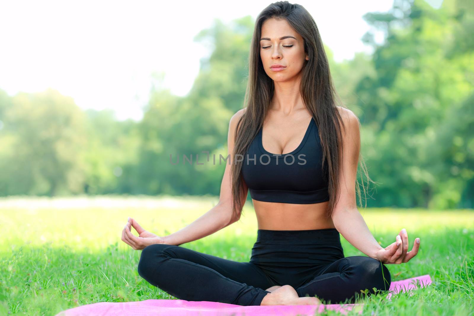 Attractive and young woman doing yoga meditation in a lotus pose outdoors in a park on a sunny day