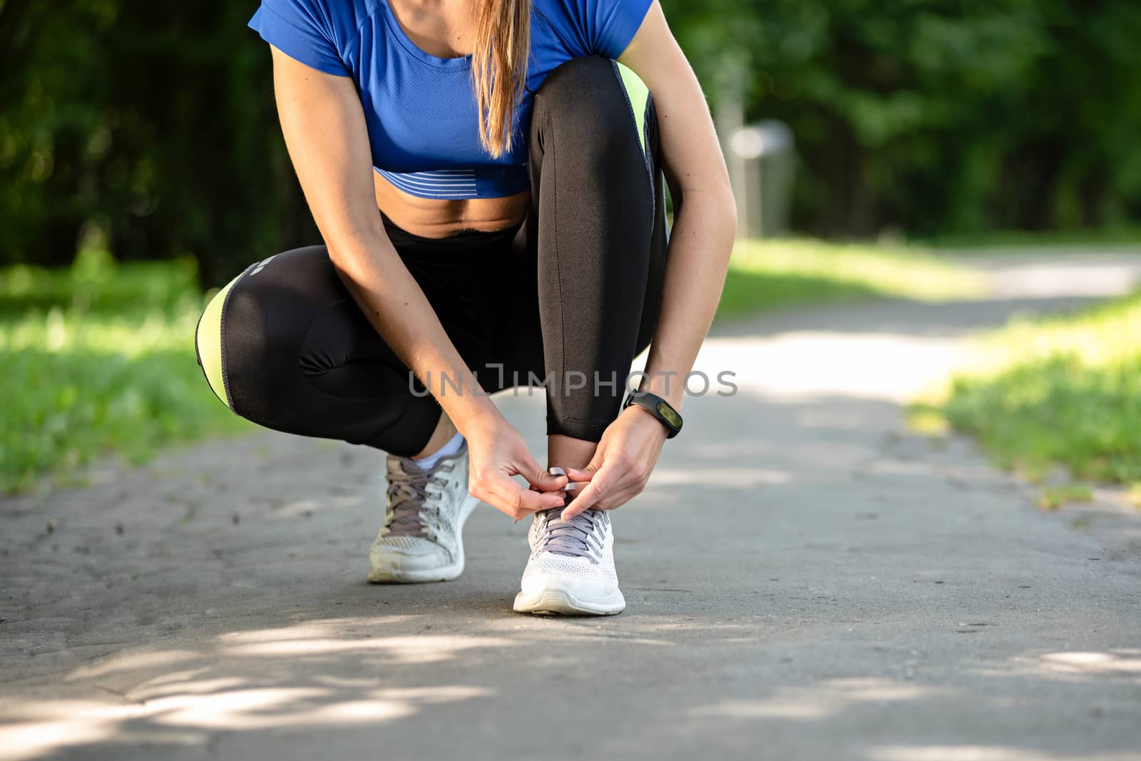 Fitness woman tying laces in running shoes during outdoors workout in the park on a sunny morning