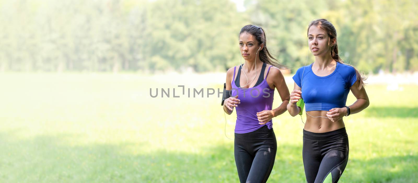 Healthy lifestyle banner - two beautiful fitness girls are jogging in the park on a sunny morning (copy space)