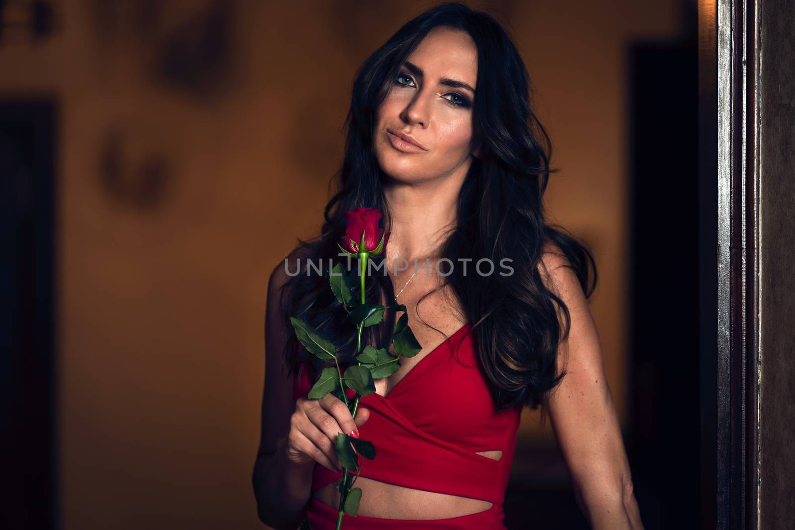 Portrait of a beautiful and elegant woman holding a rose in an evening red dress