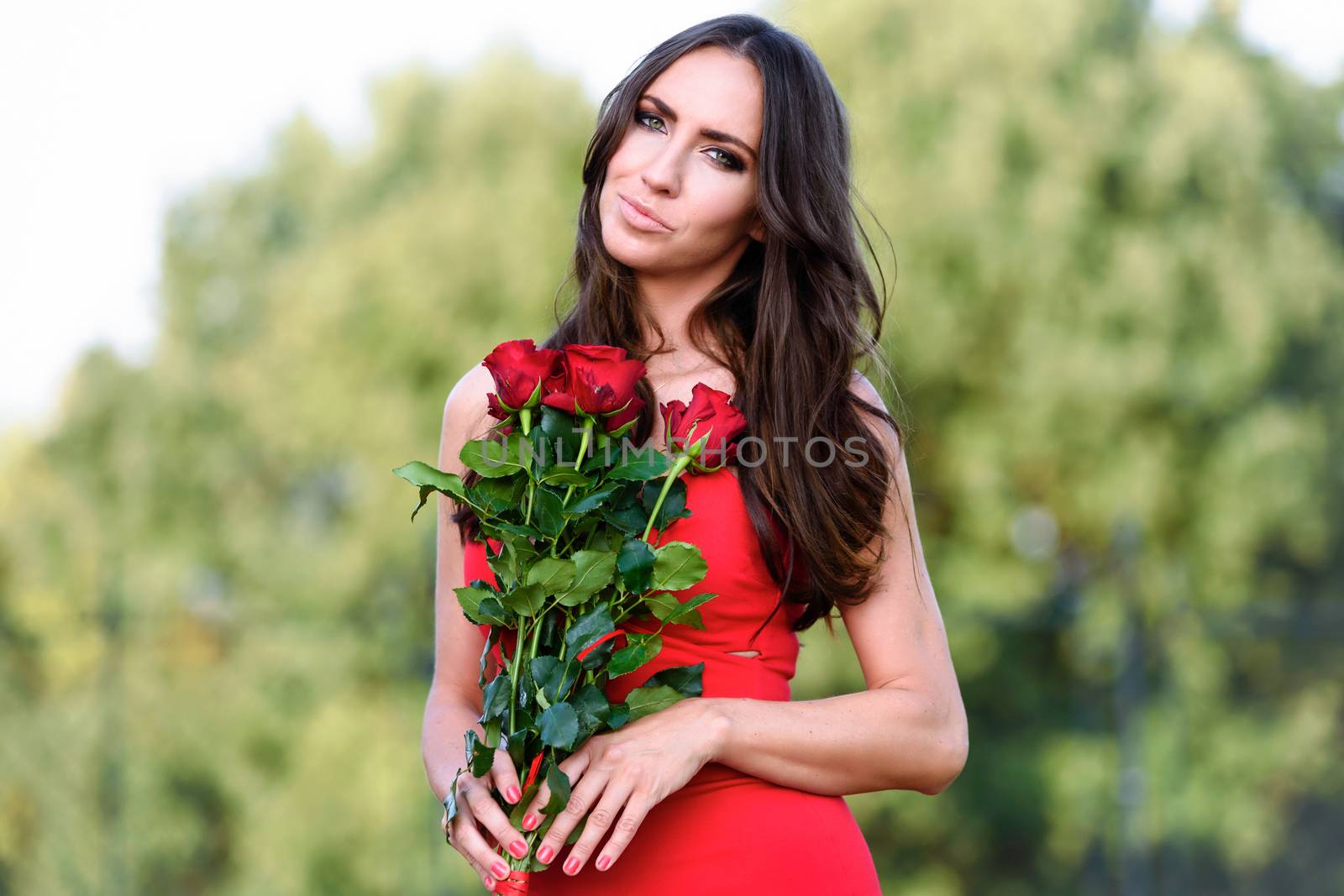 Portrait of a beautiful and elegant woman holding a bouquet of red roses on a blurred background of the garden