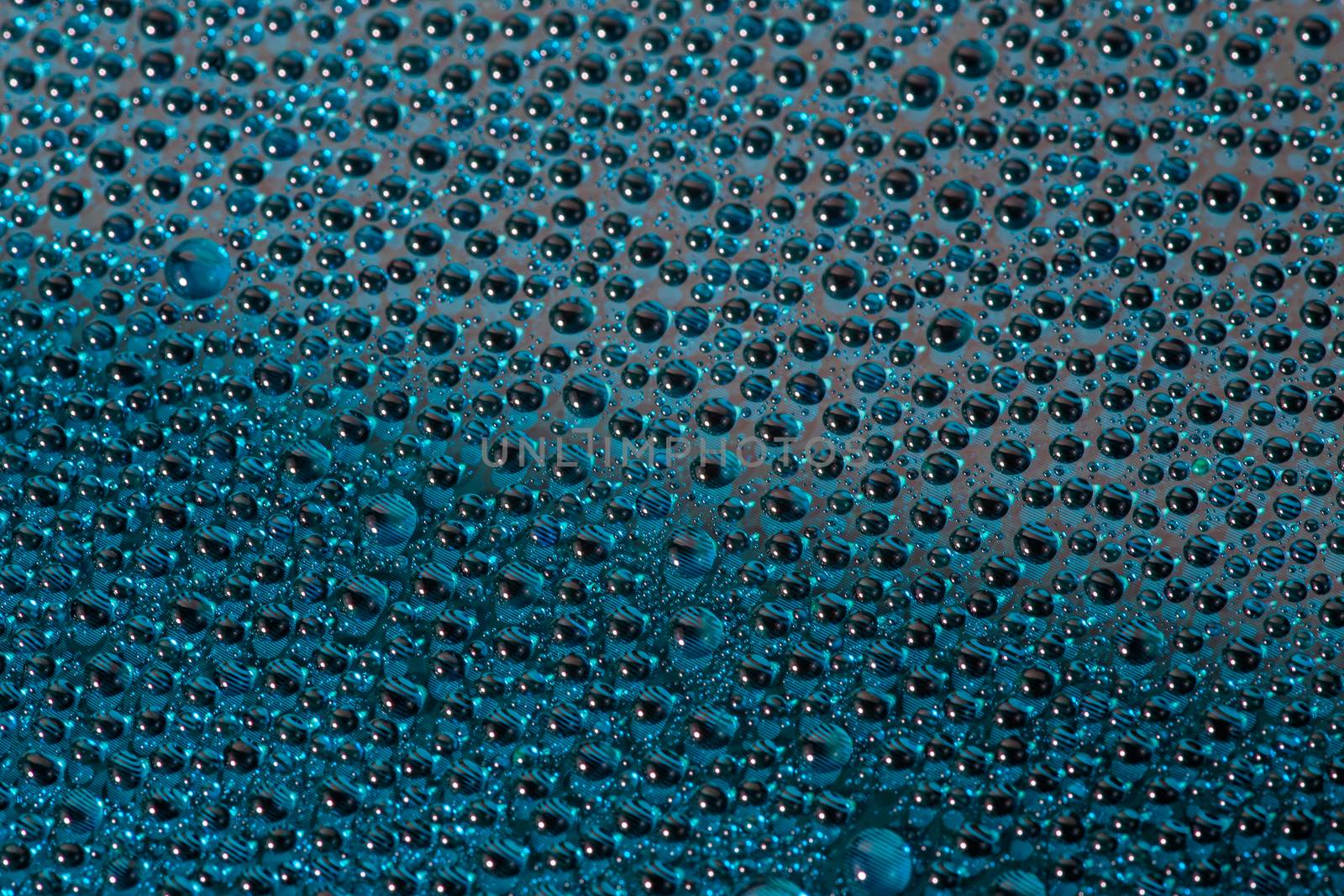 water drops on aurora green pearl glass of modern phone back cover, close-up with selective focus and blur.