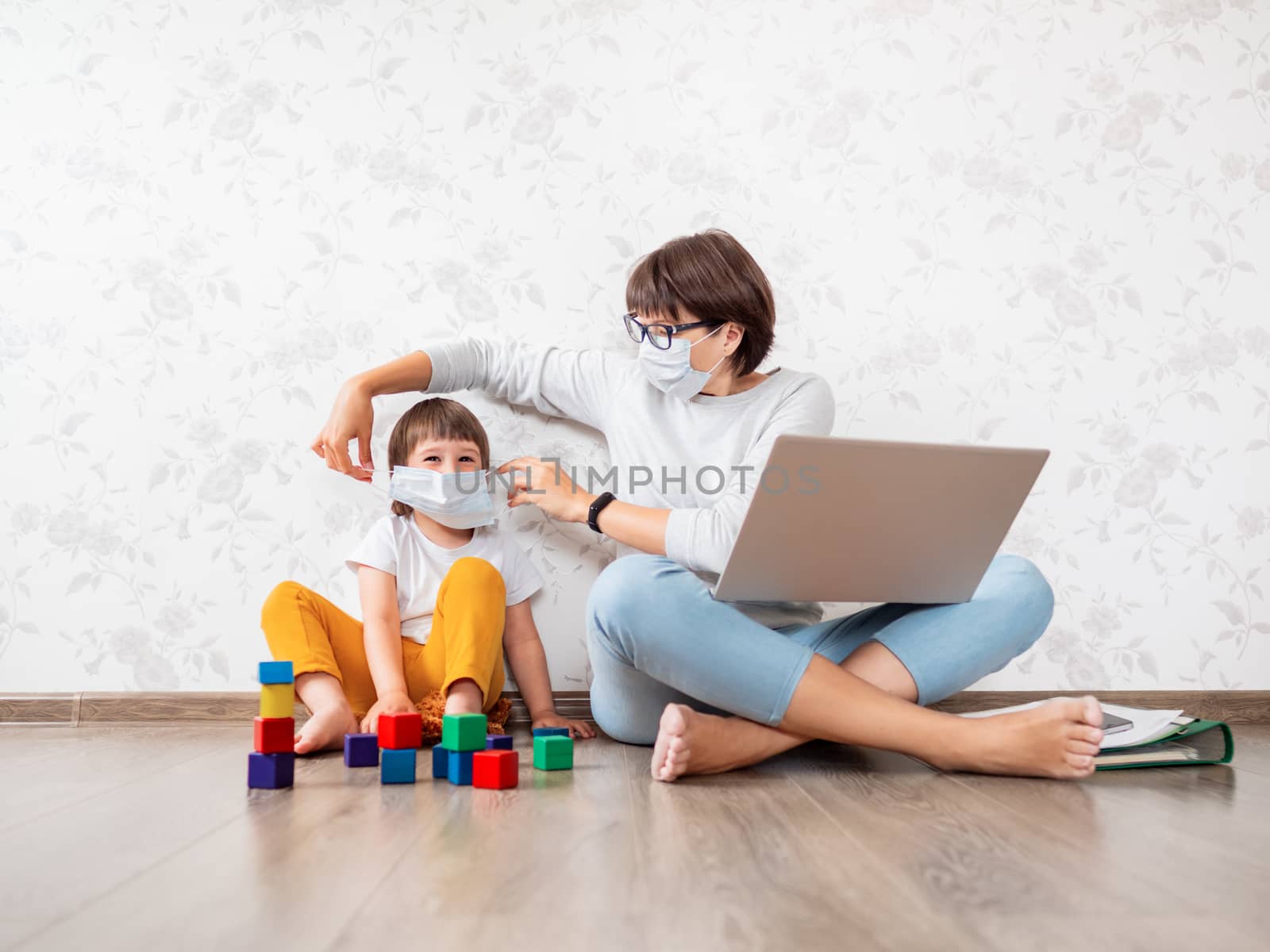 Mom and son at home quarantine because of coronavirus COVID19. Mother works remotely with laptop, son plays with toy blocks. Self isolation at home.