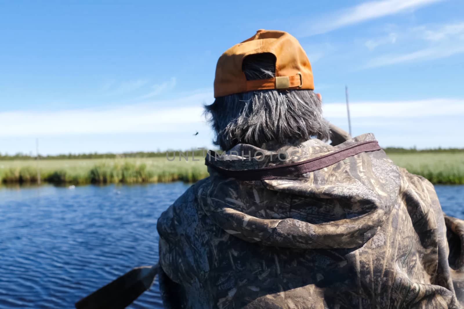 A man paddles in a boat, a view from the back.