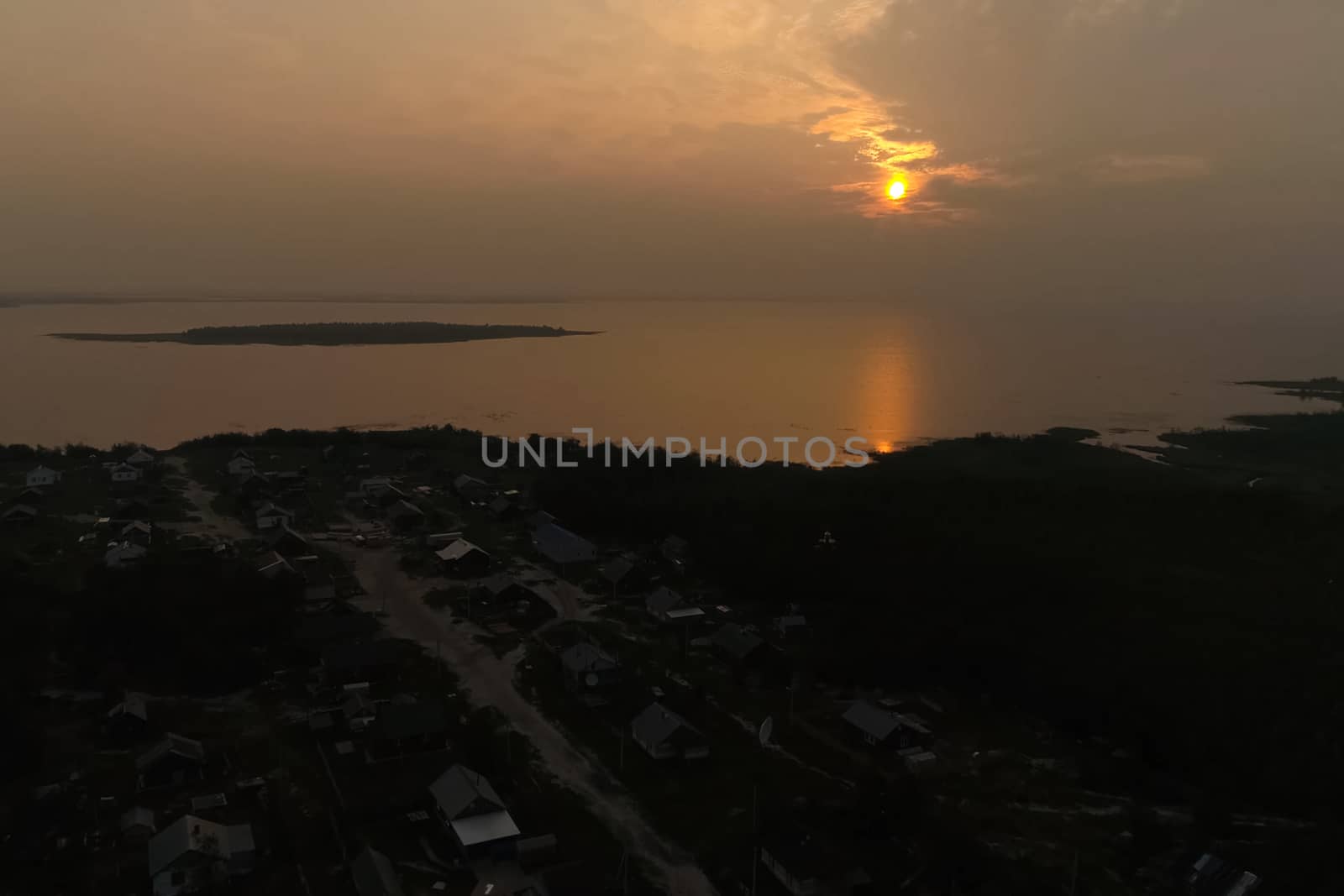 Sunny sunset over the river and the village. Twilight over the village.