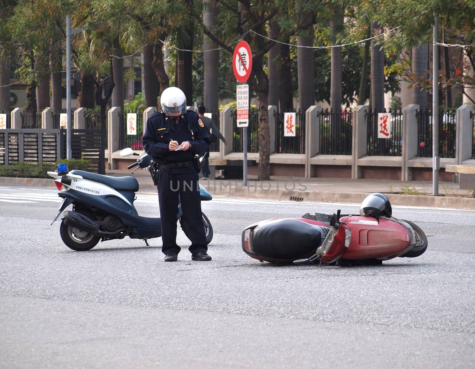KAOHSIUNG, TAIWAN -- FEBRUARY 8, 2014: A policeman records the details of a traffic accident involving a motor scooter.