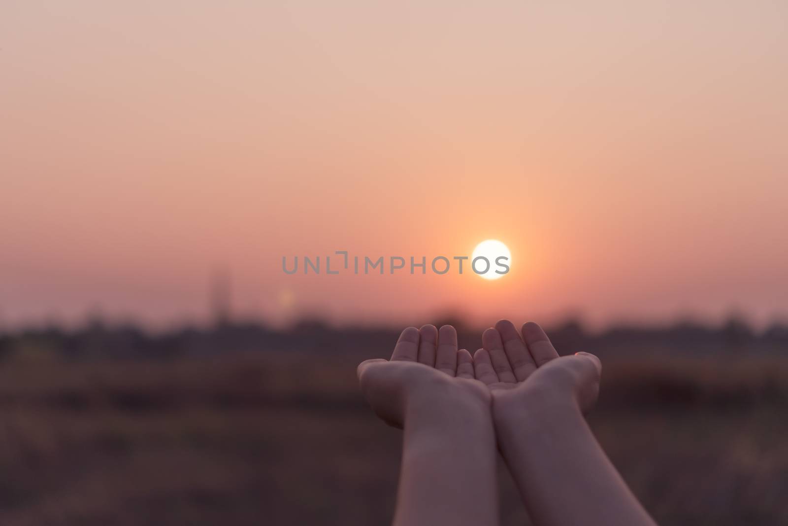 Woman hands place together like praying in front of nature blur beach sunset sky background.