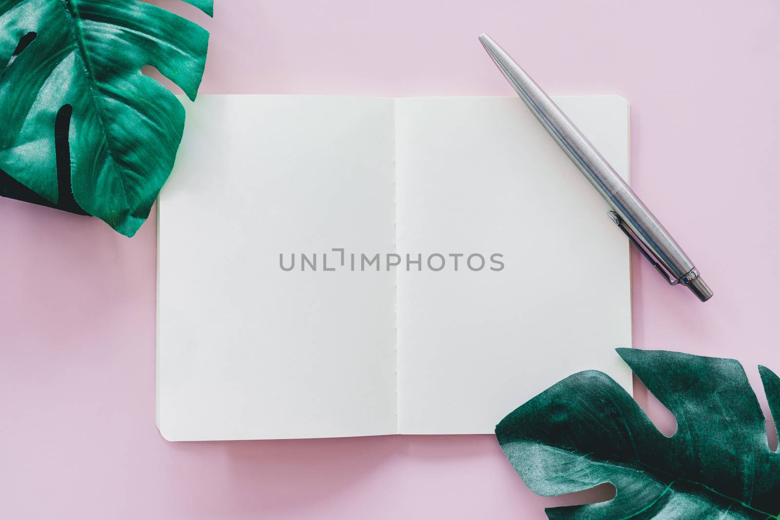 Top view of blank space white notebook and pen with tropical leaf as frame background. 