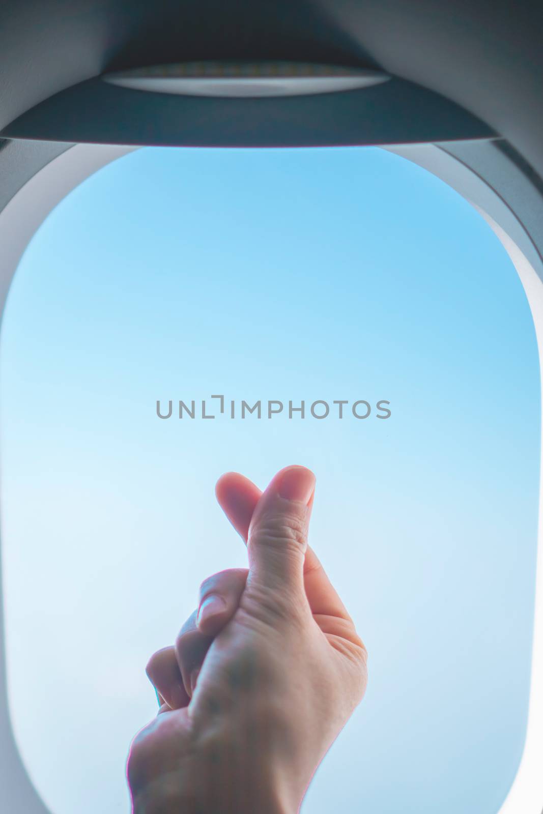 Love symbol of korean with your fingers cross. A female hand depicts a heart in front of window of airplane.  by Suwant