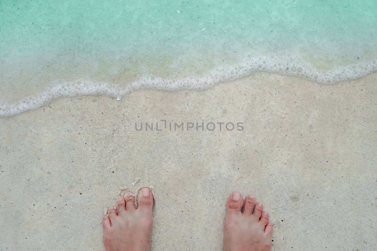 Top view of sand and water and woman foot onclean beach and white sand in summer with sun light blue sky and bokeh abstract  background.
