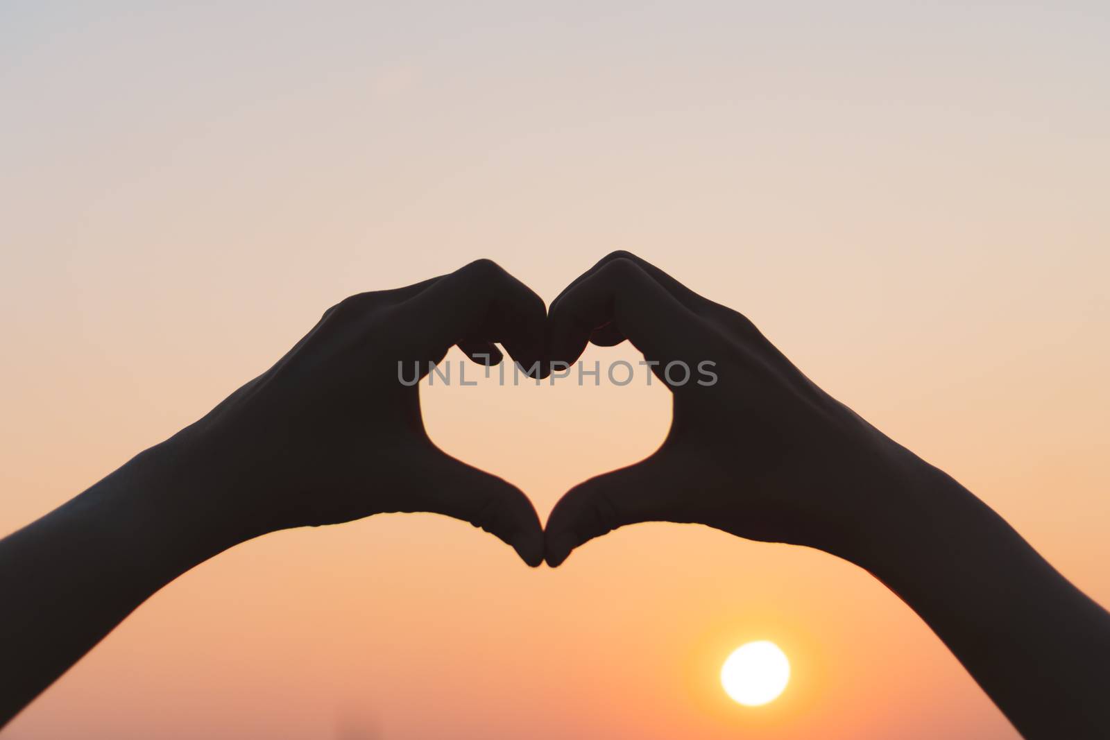 Woman hand do heart shape on sunset sky and bokeh background.