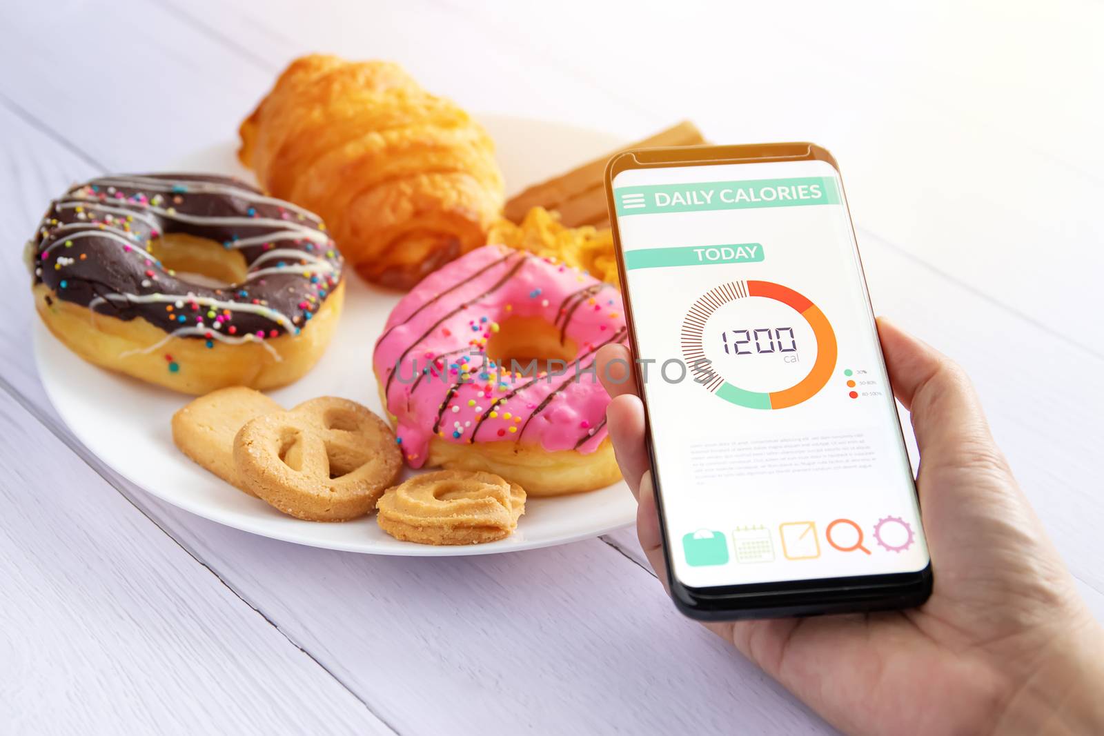 Calories counting and food control concept. woman using Calorie counter application on her smartphone with doughnut ,snack and cookies on plate at background